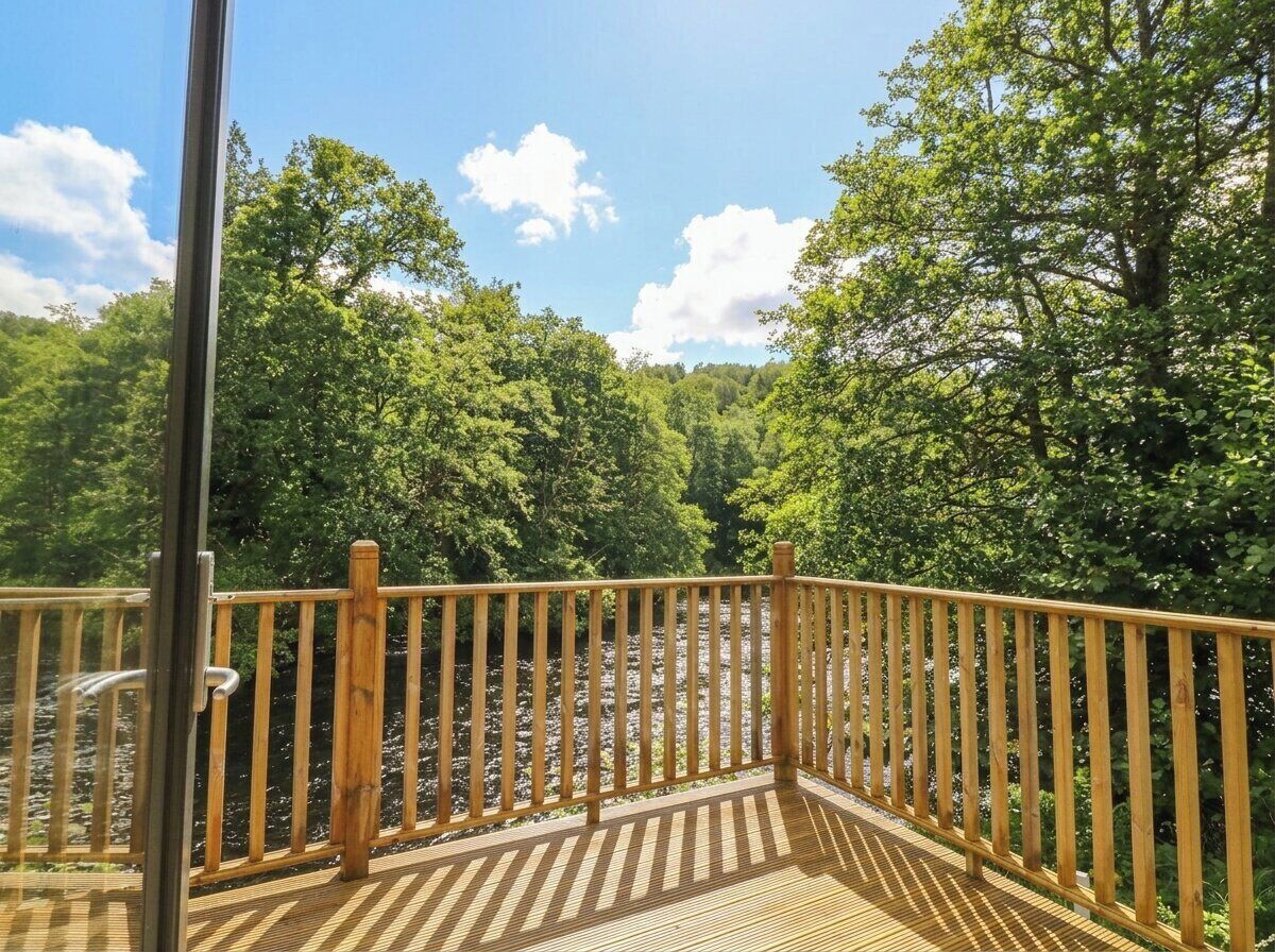 A wooden deck with a railing, surrounded by trees and a clear sky.