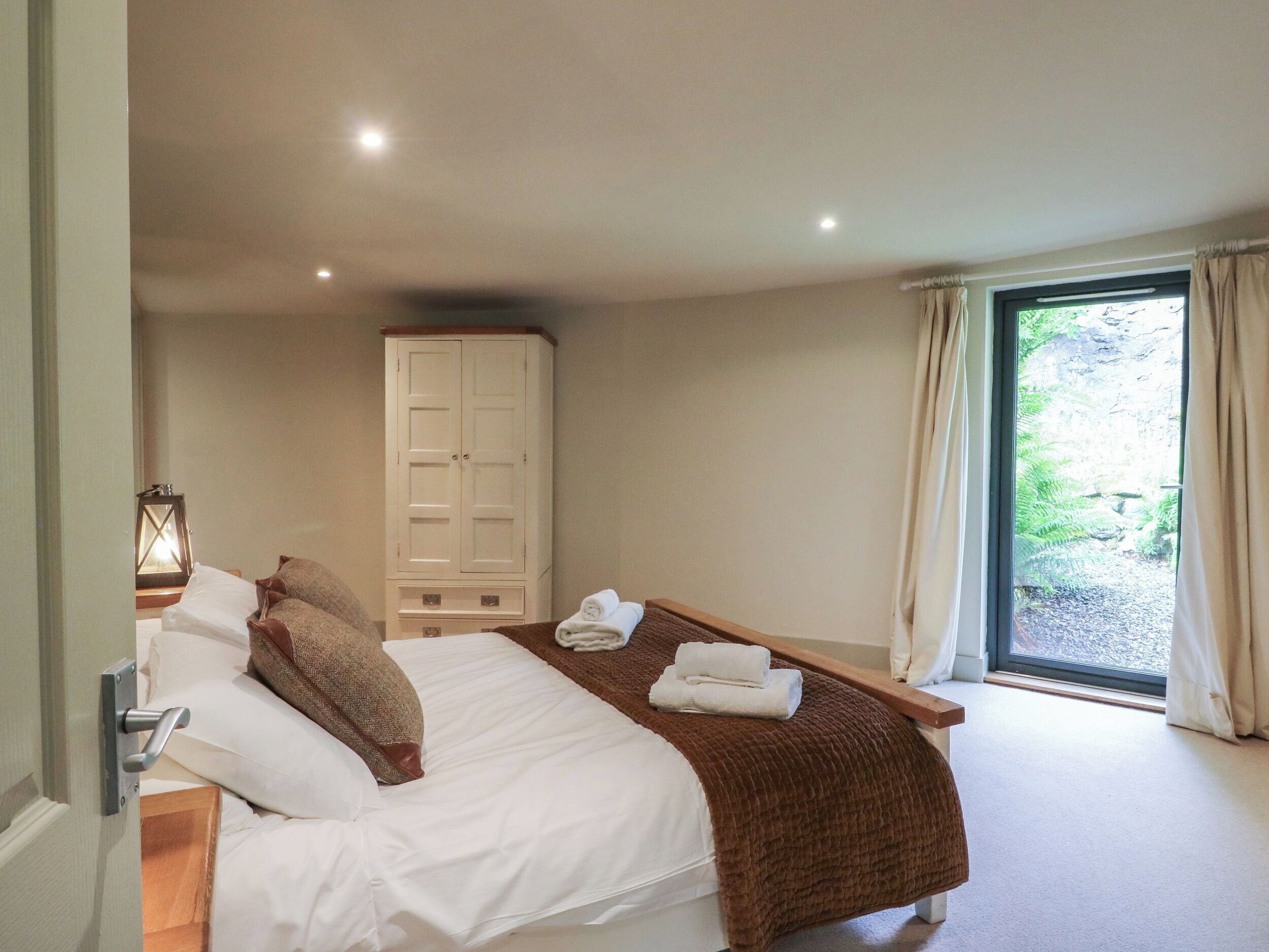 A bedroom with a bed, a wardrobe, a window with curtains, and a view of greenery outside.