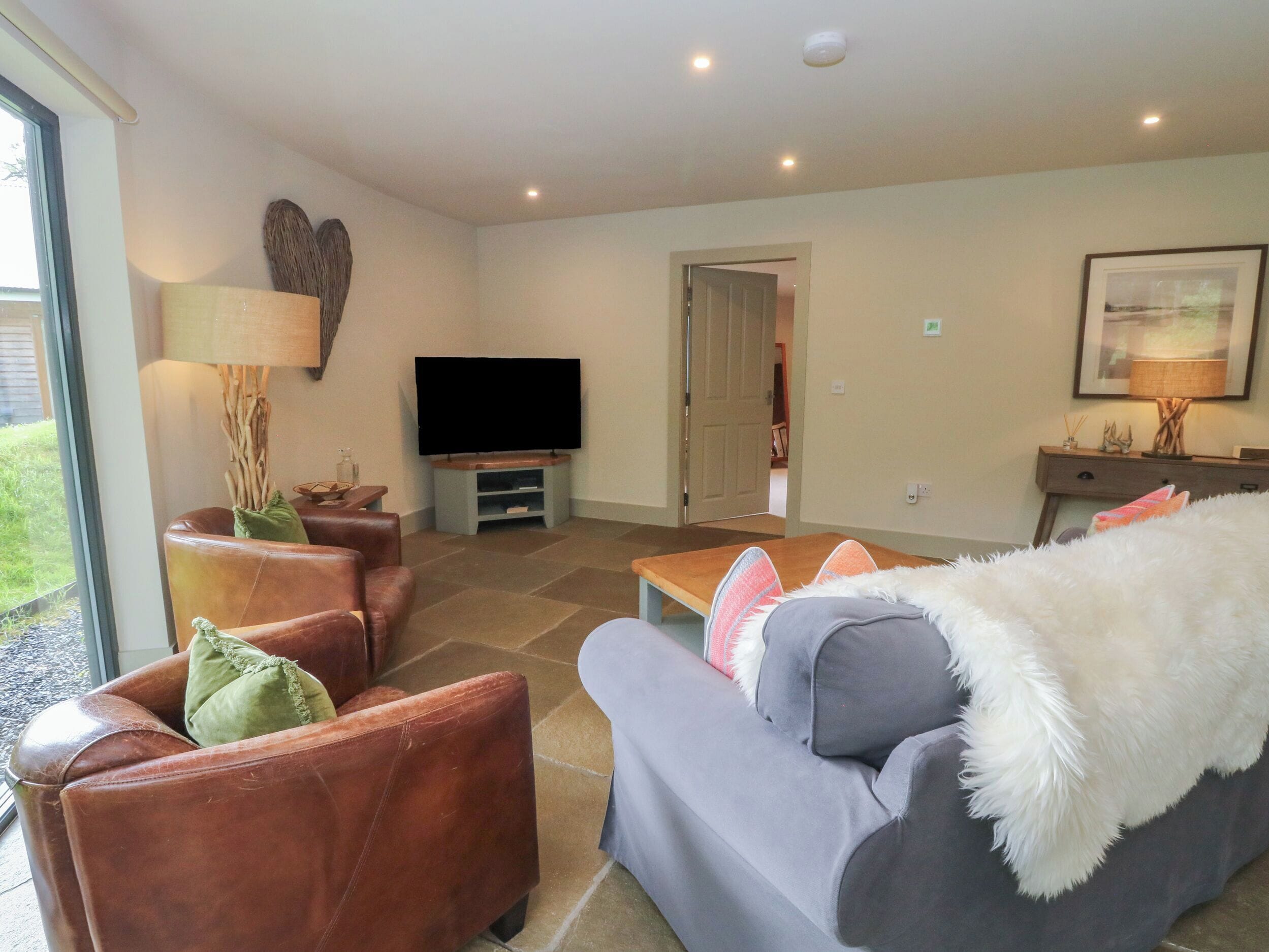 Ein Wohnzimmer mit Flachbildfernseher, Ledersessel, einem grauen Sofa und einer weißen, flauschigen Decke.