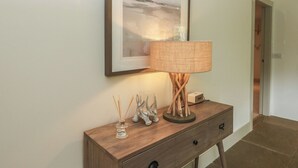 A framed artwork on a wall, a lamp on a wooden console table, and a door in the background. - The Crannog (Killin)
