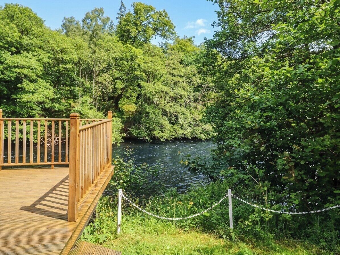 Een houten terras met uitzicht op een rivier, omringd door weelderige begroeiing.