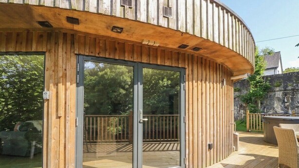 A wooden exterior with a sliding glass door, a deck, and outdoor furniture. - The Crannog (Killin)