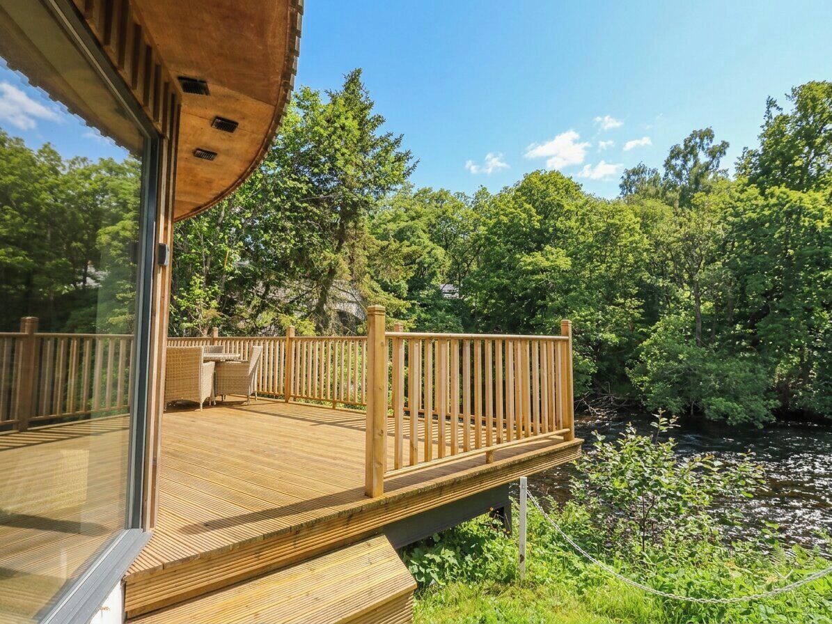 Eine Holzterrasse mit Glasumrandung, umgeben von üppiger Vegetation und einem Fluss.