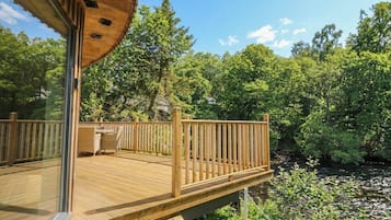 Eine Holzterrasse mit Glasumrandung, umgeben von üppiger Vegetation und einem Fluss.