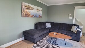 A living room with a sectional sofa, a coffee table, a painting, and a door leading to another room. - Pet-Friendly Duluth Basecamp Near Spirit Mountain (Duluth)