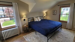 A bedroom with a bed, two bedside lamps, a radiator, a TV, and a window with curtains. - Pet-Friendly Duluth Basecamp Near Spirit Mountain (Duluth)