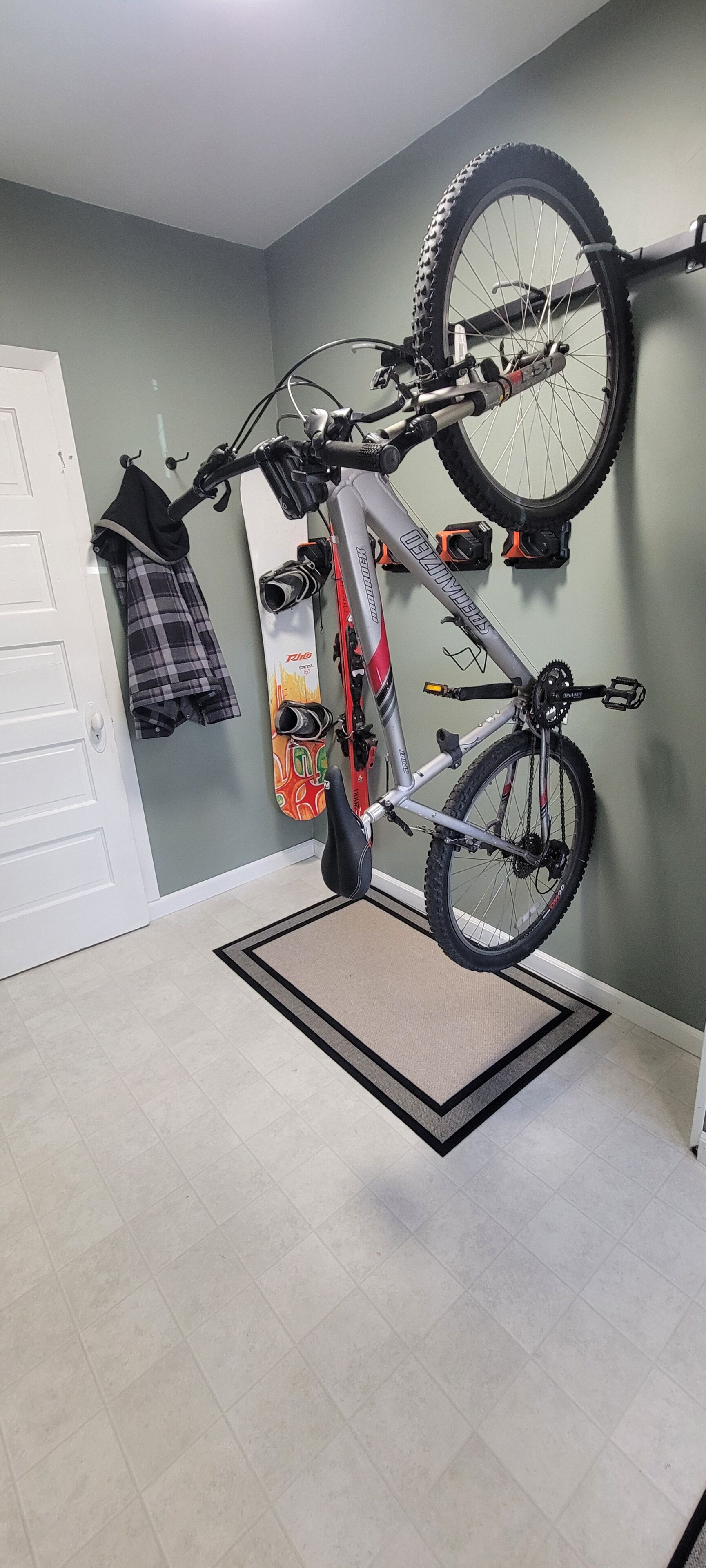 A bicycle mounted on a wall in a room with a door, a doormat, and a wall-mounted rack.