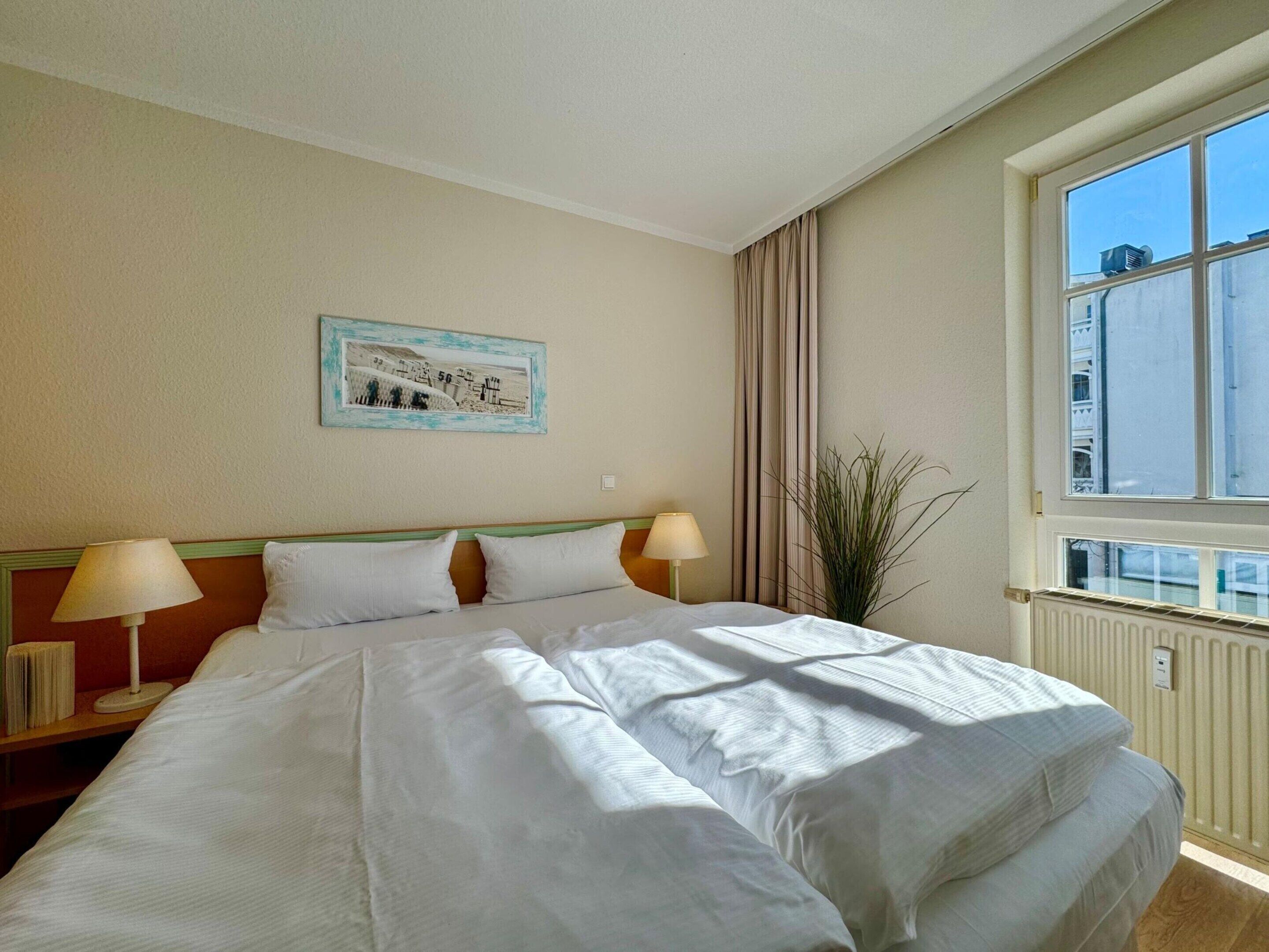 Habitación de hotel con una cama grande, dos lámparas de noche, un ventanal con vistas y un cuadro en la pared.
