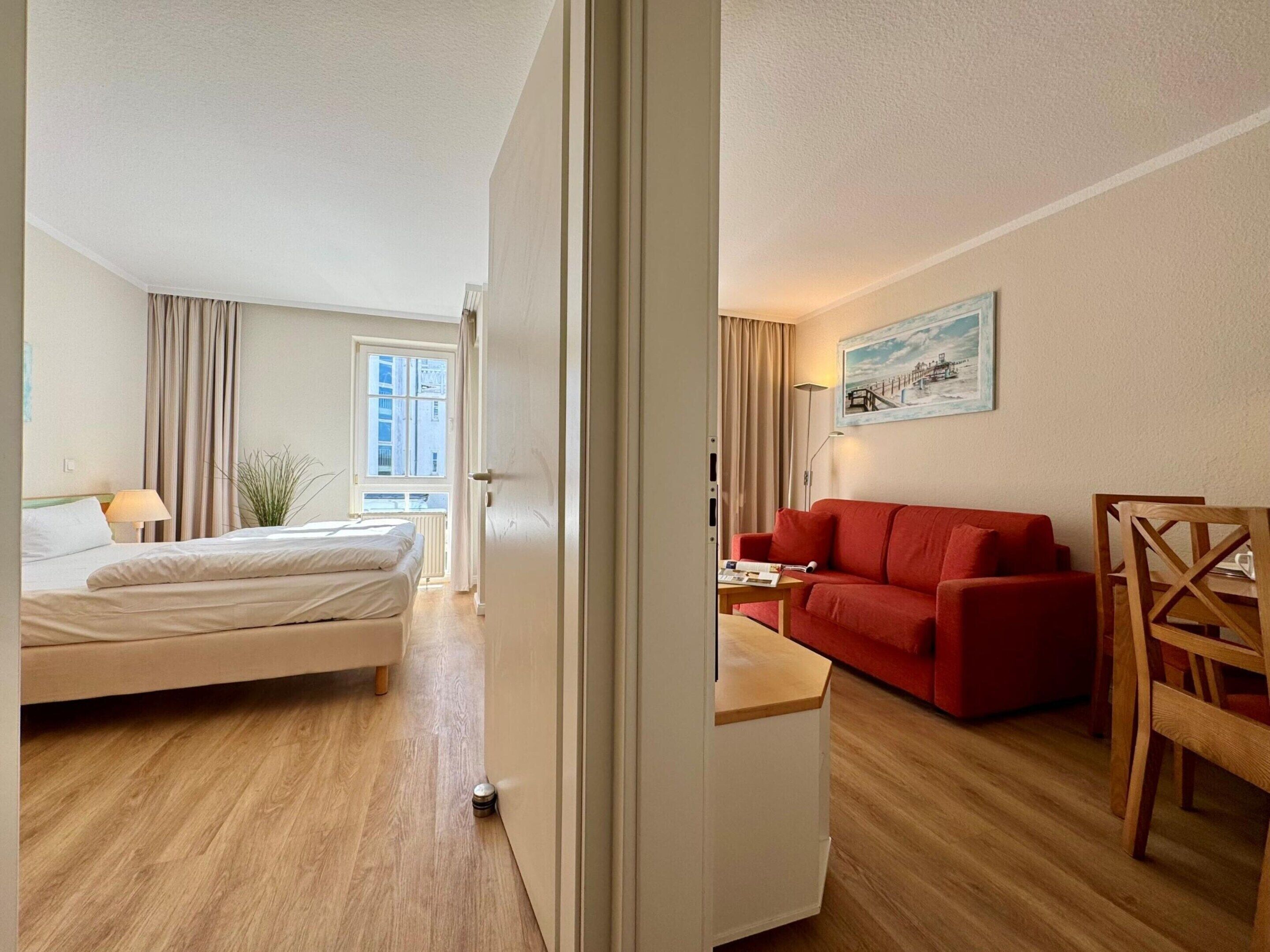 A hotel room with a bed, a red sofa, a wooden table, and a painting on the wall.