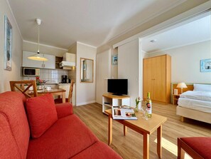 A modern living room with a red sofa, a wooden coffee table, a TV, and a kitchen in the background. - Ferienwohnung im Seepark Sellin auf Rugen Nahe Ostseestrand (Sellin)