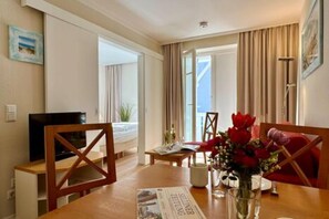 Ein Hotelzimmer mit Esstisch, Stühlen, einem Fernseher und einem Fenster mit Vorhängen.