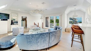 Un salon moderne avec un canapé bleu aux lignes courbes, une table basse en verre et un coin repas blanc.