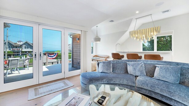Un salon moderne avec un canapé bleu, une table basse en verre et une vue sur une maison, visible à travers de grandes portes coulissantes.