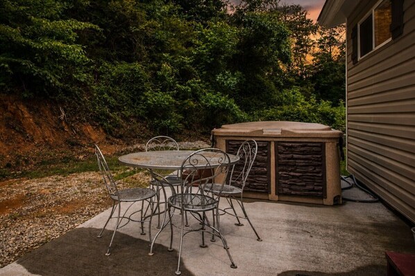 A patio with a round table and chairs, a stone fireplace, and a house in the background.