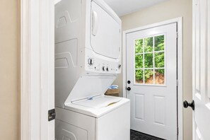 Une buanderie équipée d’un lave-linge et d’un sèche-linge à chargement frontal, d’une porte avec une fenêtre et d’un panier à linge posé sur le sol.