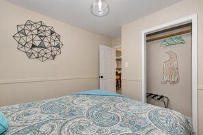 A bedroom with a patterned bedspread, a geometric wall decoration, and a closet with hangers.