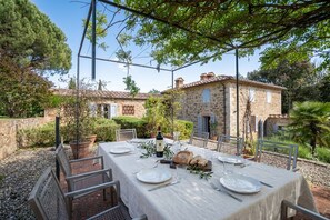An outdoor dining area with a table set for two, surrounded by stone buildings and greenery. - Private Tuscan Villa | Infinity Pool & Views (Toscana)