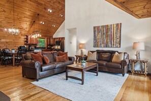 A spacious living room with a large brown leather sofa, a wooden coffee table, and a dining area with wooden chairs and a table. - Hot Tub, Views, Firepit, Fireplace, Game Room (Banner Elk)