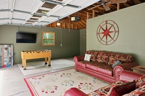 A cozy room with a red leather sofa, a wooden foosball table, a wall-mounted TV, and a large compass decoration. - Hot Tub, Views, Firepit, Fireplace, Game Room (Banner Elk)