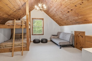 Ein Schlafzimmer im Loft-Stil mit Etagenbett, einer Schlafcouch, einem Holzschrank und einem Fenster mit Blick ins Grüne.