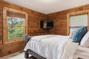 Ein Schlafzimmer einer Holzhütte mit Bett, einem montierten Fernseher und großen Fenstern.