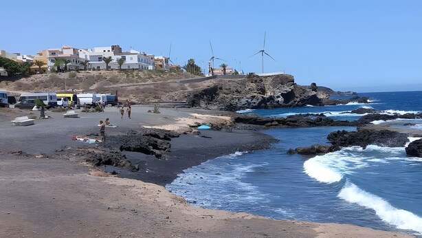 Une zone côtière avec une plage rocheuse, des éoliennes et des bâtiments en arrière-plan.