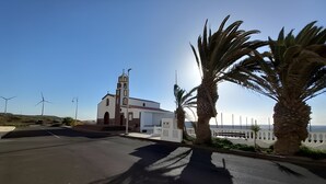 Un bâtiment situé sur la côte, doté d’un clocher, entouré de palmiers et avec des éoliennes en arrière-plan.