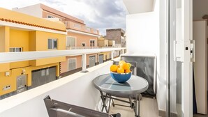 Un balcon avec un saladier de fruits, une table en verre et une vue sur les immeubles voisins.