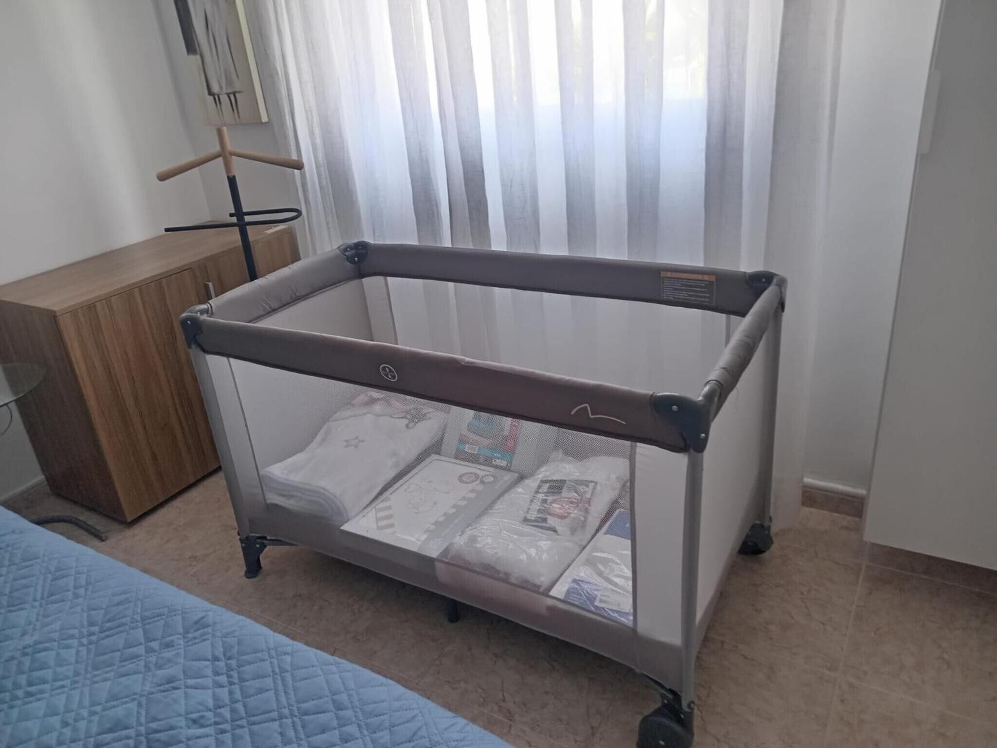 A room with a crib, a wooden cabinet, and a bed.