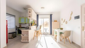 Une cuisine moderne avec des meubles de couleur verte, un coin repas avec deux chaises et une porte-fenêtre coulissante donnant sur un balcon.