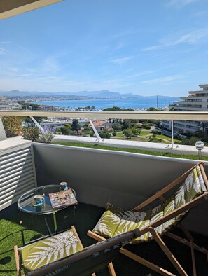 Ein Balkon mit Meerblick, ein Tisch mit einer Zeitschrift und zwei Stühle.