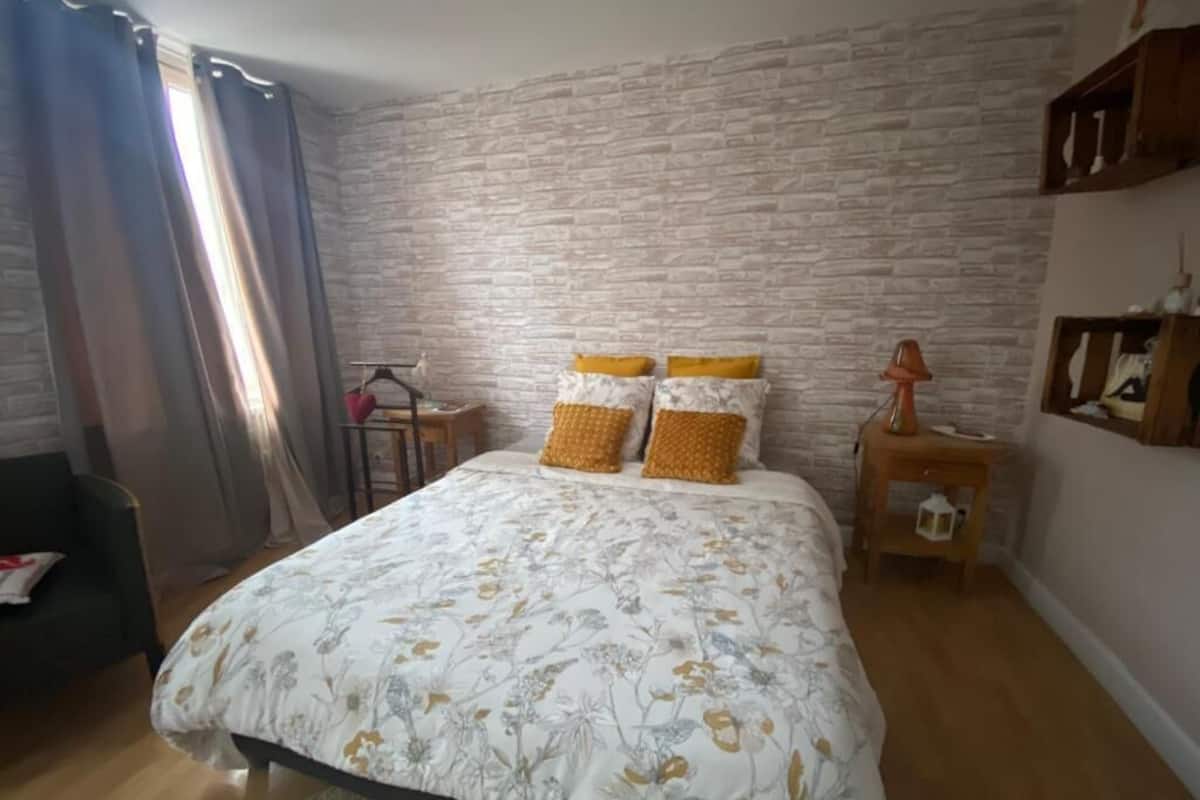 Un dormitorio con cama, mesita de noche, cómoda y ventana con cortinas.