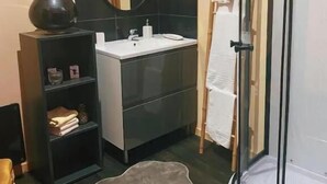 Une salle de bain avec une douche à parois de verre, un lavabo, un miroir, une étagère avec des livres et un tapis.