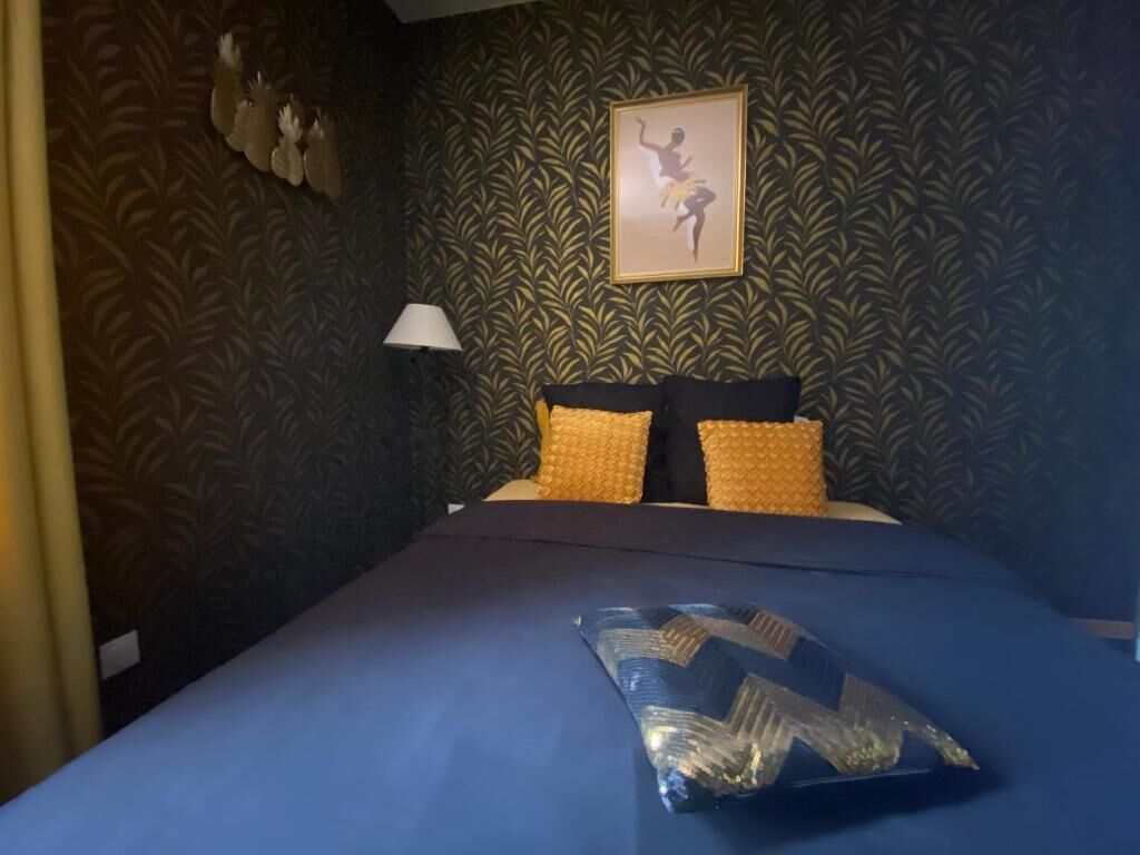 A hotel room with a bed, a wall with a leaf pattern, a framed picture, and a nightstand with a lamp.