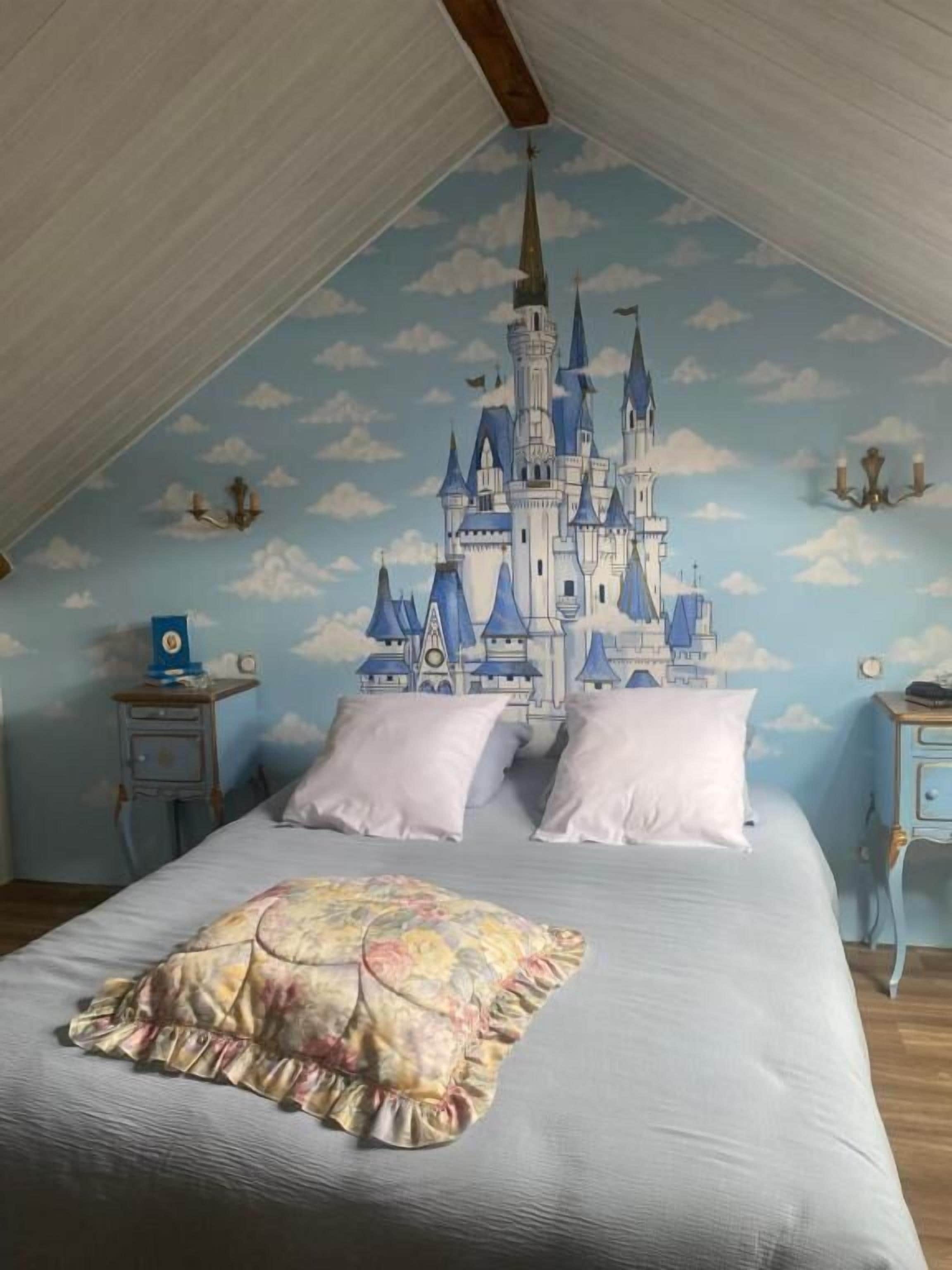 Un dormitorio con un mural de castillo, una cama con colcha floral y dos mesitas de noche con lámparas.