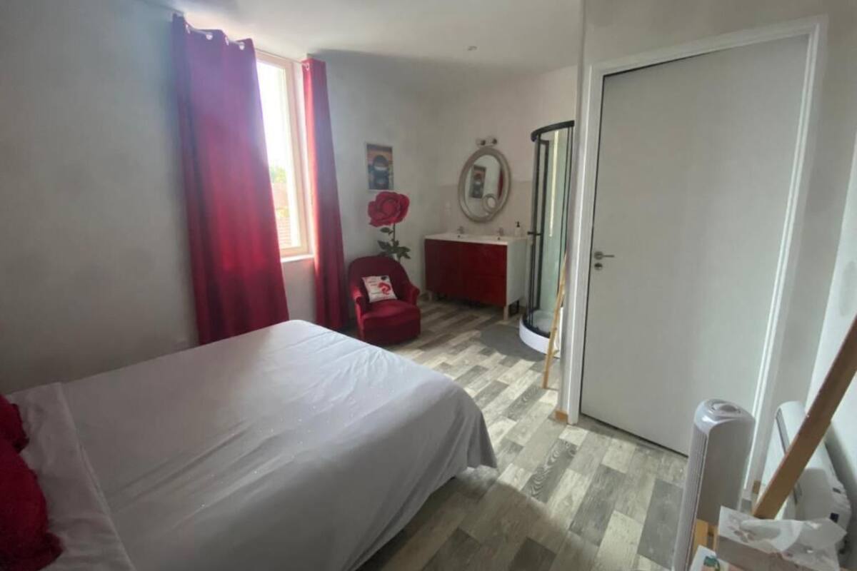 Un dormitorio con cama, una silla, una mesita, un espejo y una puerta.