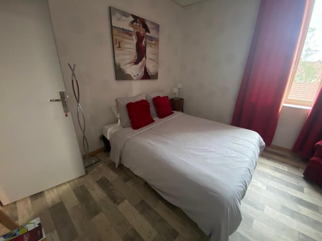 A bedroom with a bed, a painting on the wall, and a window with curtains.