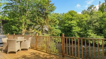 A wooden deck with wicker furniture, a wooden railing, and a river view.