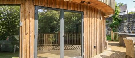 Un edificio de madera con puerta de vidrio, una terraza y mobiliario exterior.
