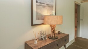 A framed picture on a wall, a lamp on a wooden console table, and a door in the background. - Otters Holt (Killin)