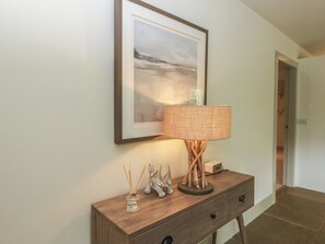 A framed picture on a wall, a lamp on a wooden console table, and a door in the background.
