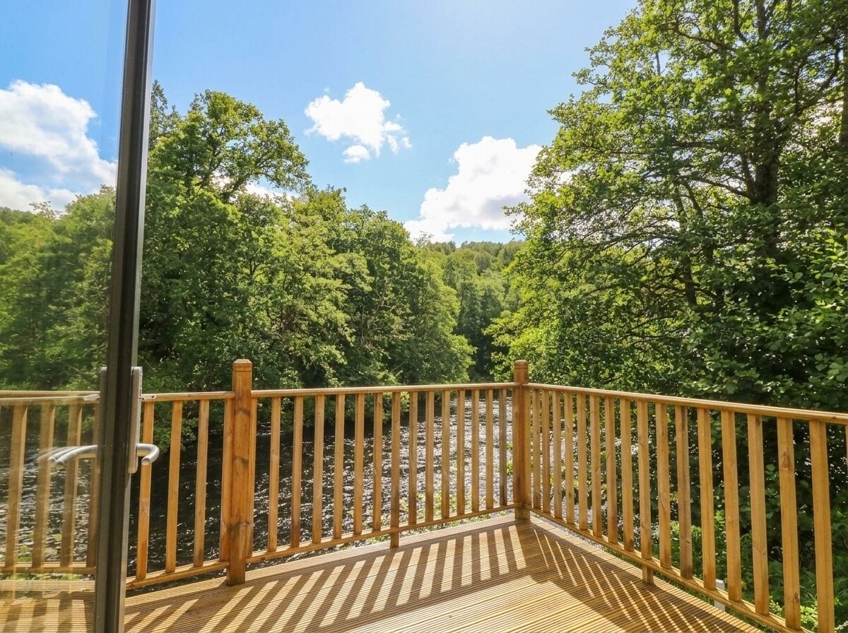 Un terrazza in legno con ringhiera che si affaccia su una zona boschiva.