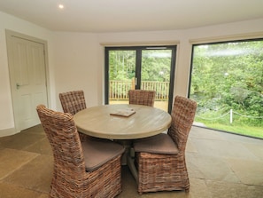 A round table with four wicker chairs, a white door, and a view of greenery through large windows. - Otters Holt (Killin)