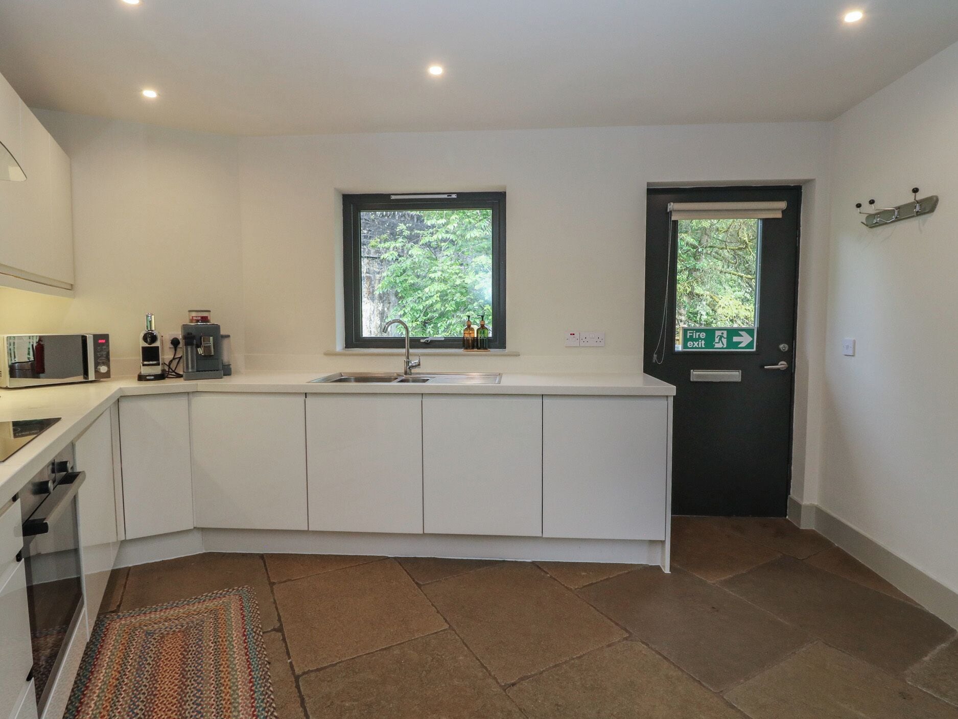 Una cocina moderna con armarios blancos, microondas integrado, un lavamanos y una ventana.