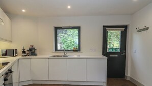 A modern kitchen with white cabinets, a built-in microwave, a sink, and a window. - Otters Holt (Killin)