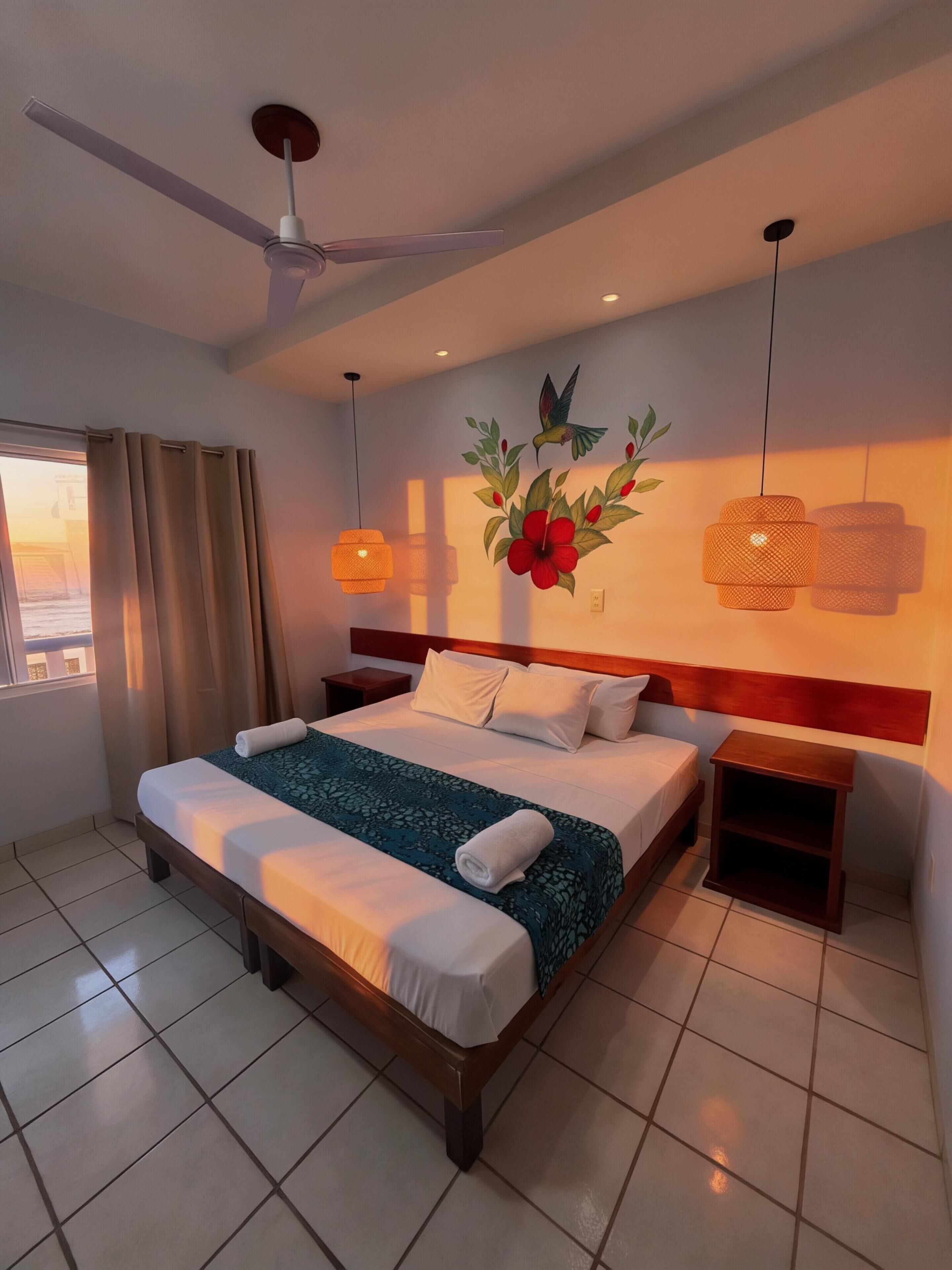 A hotel room with a bed, a nightstand, a ceiling fan, a window with curtains, and a wall decoration.