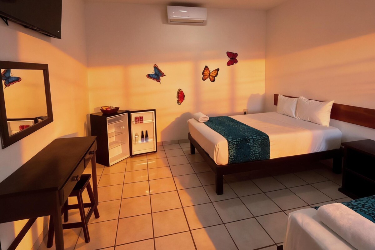 Habitación de hotel con cama, escritorio, silla, ventilador de techo y aire acondicionado.