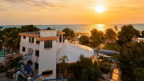 Un edificio residencial con piscina, rodeado de palmeras y vista al mar al atardecer.