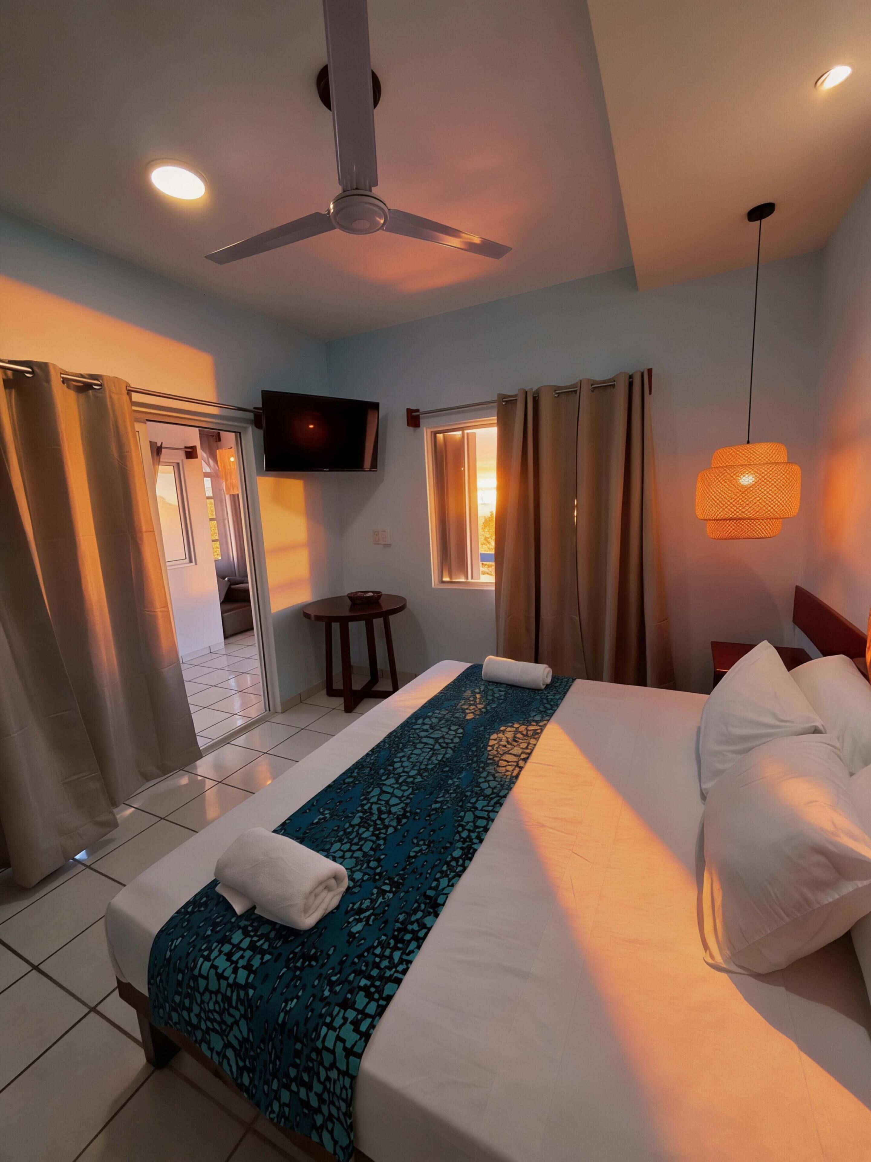 Habitación de hotel con cama, cortinas, ventilador de techo, televisión y una mesita.