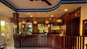 Un hall de hotel con mostrador de recepción, ventilador de techo y un perro acostado en el suelo.